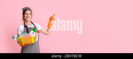 Femme de ménage souriante tenant le panier avec des fournitures de nettoyage et pointant vers l'espace de copie Banque D'Images