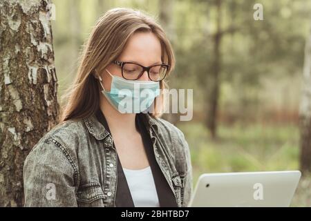 Indépendant pendant la quarantaine dans la nature. Femme en masque travaille sur un ordinateur portable en forêt. Concept de travail à distance Banque D'Images