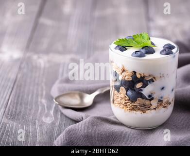 Yaourt blanc dans un pot en verre avec bleuets sur fond gris. Banque D'Images