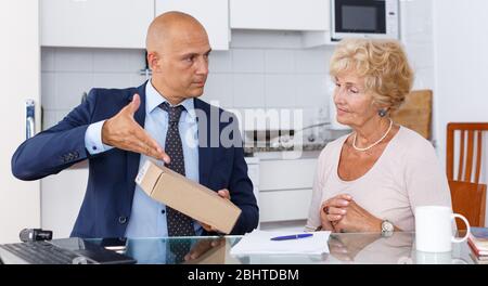 Agent de vente montrant boîte en carton avec marchandises mature woman in kitchen Banque D'Images