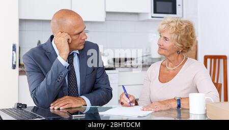 Femme mature et d'remplit dans les documents pour l'achat de biens dans la cuisine Banque D'Images