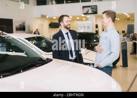 Un client heureux et un vendeur sympathique discutent de la nouvelle voiture dans la concession automobile. Banque D'Images