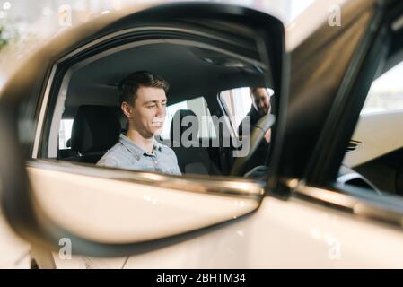 Jeune homme prêt à acheter une nouvelle voiture dans la concession automobile, vue de la réflexion dans le miroir. Banque D'Images