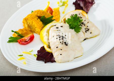 Filet de merlu cuites à la poêle avec de l'eau et l'huile d'olive pendant 10 minutes, assaisonné de sel et poivre, garnie de maïs bouilli, verts, citron Banque D'Images