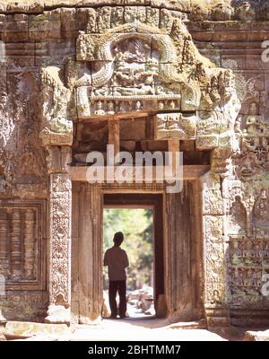 Jeune garçon debout dans l'ancienne porte, Temple Ta Prohm, Siem Reap, Royaume du Cambodge Banque D'Images