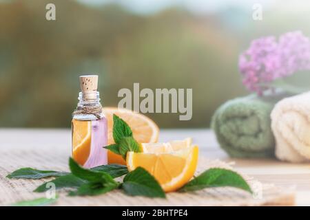 Bouteille d'huile d'orange, feuilles de menthe verte et orange sur table en bois. Serviettes pour le spa et le lilas dans un fond naturel flou. Mise au point sélective. Banque D'Images