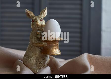 Composition printanière, figurine de lapin doré avec oeuf sur nappe beige, concept de Pâques, foyer sélectif Banque D'Images