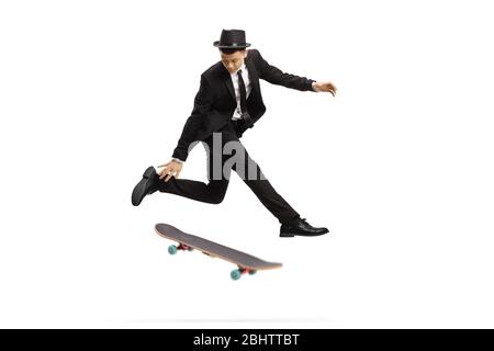 Jeune homme dans un élégant costume sautant avec un skateboard isolé sur fond blanc Banque D'Images