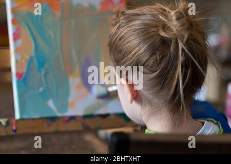 Jeune enfant travaillant sur une peinture en toile à l'aide de pinceau et son imagination aux couleurs vives Banque D'Images