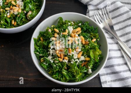 Salade de kale avec vinaigrette aux oignons doux : salade de kale avec vinaigrette aux oignons doux surmontée de fromage de chèvre émietté et de pignons grillés Banque D'Images