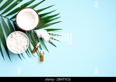 Huile essentielle de noix de coco sur fond bleu avec la moitié de noix de coco, la noix de coco tranché dans le bol et la feuille de palmier tropicale. Plat, vue du dessus. SPA biologique naturel Banque D'Images