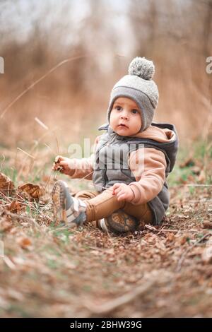 un petit garçon est assis sur un chemin forestier dans une gelée grise et regarde curieusement à la caméra Banque D'Images