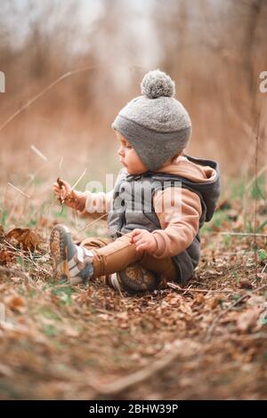 un petit garçon est assis sur un chemin forestier dans une gelée grise et regarde curieusement la nature Banque D'Images