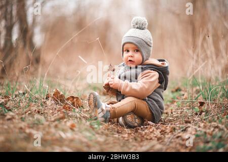 un petit garçon est assis sur un chemin forestier dans une gelée grise et regarde curieusement à la caméra Banque D'Images