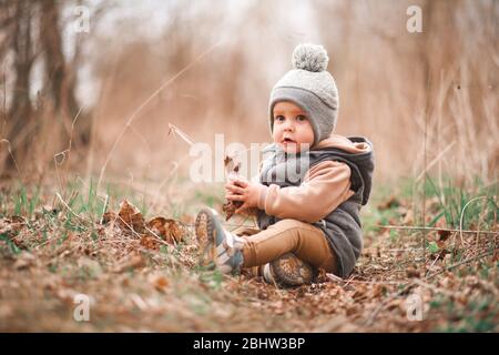 un petit garçon est assis sur un chemin forestier dans une gelée grise et regarde curieusement à la caméra Banque D'Images