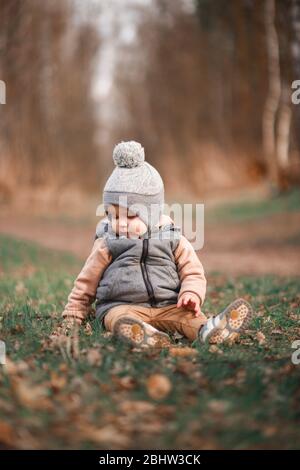 un petit garçon est assis sur un chemin forestier dans une gelée grise et regarde curieusement au sol Banque D'Images