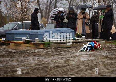 Boston, Massachusetts, États-Unis. 27 avril 2020. Le COVID-19, Corona virus, dans le Massachusetts est le troisième état le plus touché en Amérique. Une famille fait le plein de deux êtres chers dans le cimetière de Calvary dans le quartier de Dorchester à Boston, sous la pluie, le lundi 27 avril 2020. Crédit: Allison Dinner/ZUMA Wire/Alay Live News Banque D'Images