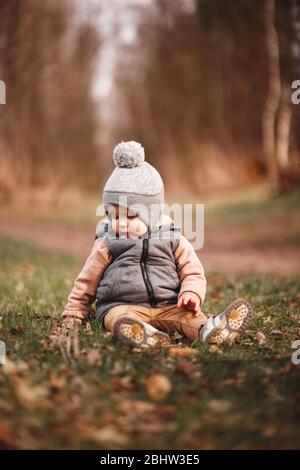 un petit garçon est assis sur un chemin forestier dans une gelée grise et regarde curieusement au sol Banque D'Images