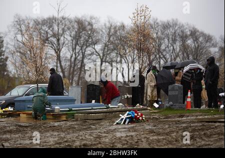 Boston, Massachusetts, États-Unis. 27 avril 2020. Le COVID-19, Corona virus, dans le Massachusetts est le troisième état le plus touché en Amérique. Une famille fait le plein de deux êtres chers dans le cimetière de Calvary dans le quartier de Dorchester à Boston, sous la pluie, le lundi 27 avril 2020. Les ouvriers du cimetière baissent le premier cercueil. Crédit: Allison Dinner/ZUMA Wire/Alay Live News Banque D'Images