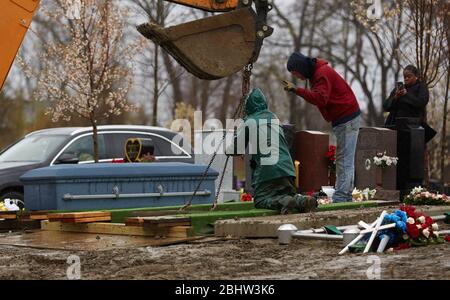 Boston, Massachusetts, États-Unis. 27 avril 2020. Le COVID-19, Corona virus, dans le Massachusetts est le troisième état le plus touché en Amérique. Une famille fait le plein de deux êtres chers dans le cimetière de Calvary dans le quartier de Dorchester à Boston, sous la pluie, le lundi 27 avril 2020. Les ouvriers du cimetière baissent le premier cercueil. Crédit: Allison Dinner/ZUMA Wire/Alay Live News Banque D'Images