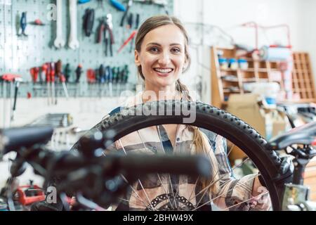 Mécanicien vélo femme regardant à travers la roue de bicyclette Banque D'Images