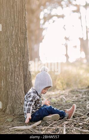 Tout-petit garçon assis contre un arbre dans les bois Banque D'Images