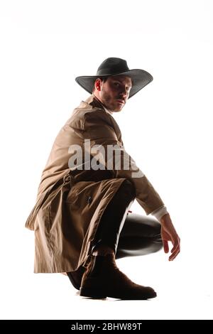 Portrait d'un jeune homme de belle qualité portant un pantalon noir en cuir et un manteau beige isolé sur fond blanc Banque D'Images