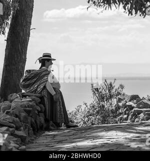 Photo en noir et blanc d'une femme indigène péruvienne quechua reposant contre un mur sur l'île Taquile, lac Titicaca, Pérou. Banque D'Images