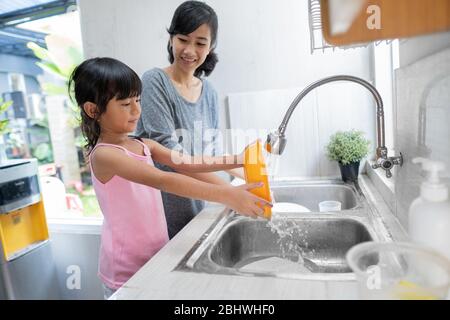 Aide à la main. Petite fille mignon aide sa mère dans les plats de lavage à la cuisine familiale Banque D'Images