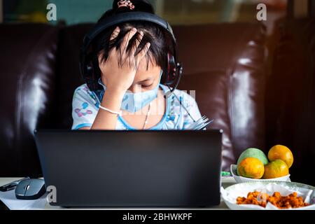 Stress Little School girl est étude à la maison avec ordinateur portable et masque de visage.concept d'éducation en ligne Banque D'Images