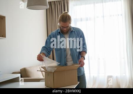 Jeune homme client ouvrir boîte en carton déballage après la livraison du courrier à la maison. Banque D'Images