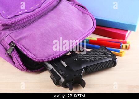 Pistolet dans le sac à dos de l'école sur table en bois, sur fond lumineux Banque D'Images