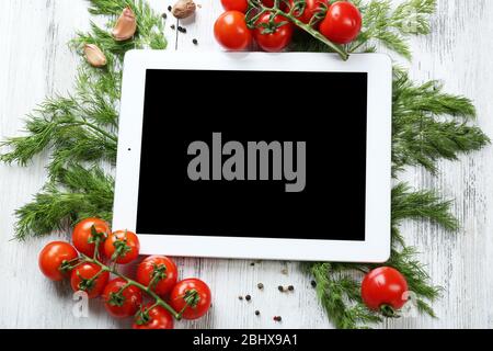 Comprimé numérique avec herbes fraîches, tomates et épices sur fond en bois Banque D'Images