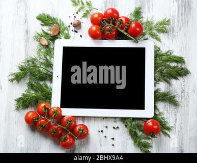 Comprimé numérique avec herbes fraîches, tomates et épices sur fond en bois Banque D'Images