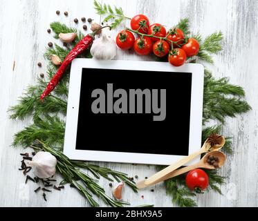 Comprimé numérique avec herbes fraîches, tomates et épices sur fond en bois Banque D'Images