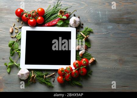 Comprimé numérique avec herbes fraîches, tomates et épices sur fond en bois Banque D'Images