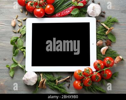 Comprimé numérique avec herbes fraîches, tomates et épices sur fond en bois Banque D'Images