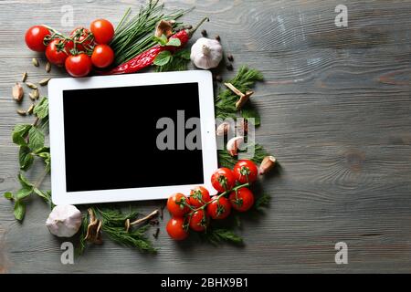 Comprimé numérique avec herbes fraîches, tomates et épices sur fond en bois Banque D'Images