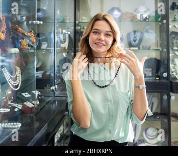 Portrait de la jeune femme heureuse choisissant rouge foncé perles collier en magasin Banque D'Images