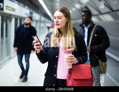 Portrait de la femme en train sur la plate-forme du métro et lecture des horaires au téléphone Banque D'Images