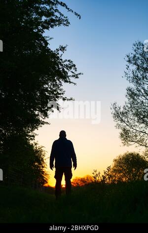 Homme marchant le long d'un chemin de remorquage près du canal d'oxford au lever du soleil. Oxfordshire, Angleterre. Silhouette Banque D'Images