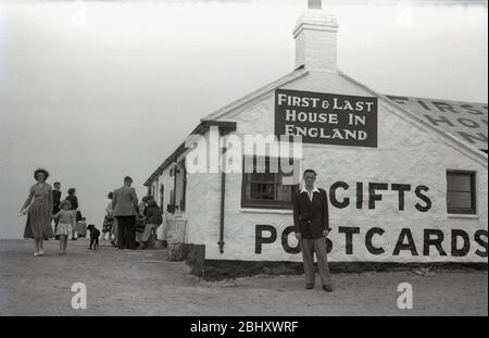 Années 1950, historique, un gentleman dans une chemise à col ouvert, un blazer et des pantalons debout pour une photo à l'extérieur de la célèbre 'First & Last House' à Lands End, Cornwall, un vieux cottage à un étage qui vendait des visiteurs de la côte, des rafraîchissements, des cadeaux, des souvenirs et des cartes postales, Angleterre, ROYAUME-UNI. Banque D'Images