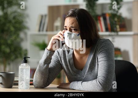 Une jeune fille inquiète dans le confinement du coronavirus appelle sur un smartphone portant un masque de protection à la maison dans la nuit Banque D'Images