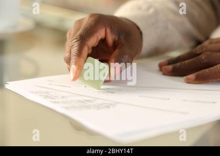 Gros plan sur les mains noires de l'homme gommant le dessin avec du caoutchouc sur un bureau à la maison Banque D'Images