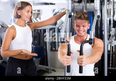 Beau homme bien formé utilisant les machines de gym de plate-forme pec tout en écoutant la petite amie à l'intérieur Banque D'Images