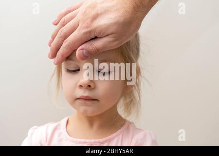 la main de l’homme se trouve sur le front d’une jeune fille de trois ans. Le père vérifie la température du corps de l’enfant. Fièvre du virus Banque D'Images