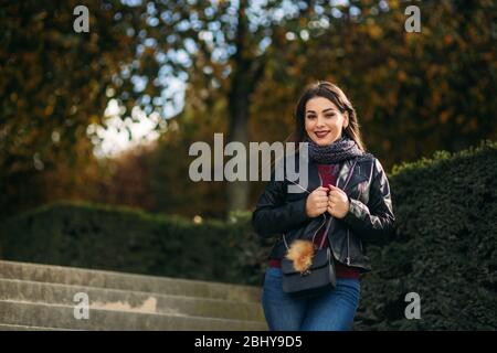 Jolie dame dans une veste en cuir noir avec un sac noir et un chemisier bordeaux. Jeune femme séduisante sourire Banque D'Images