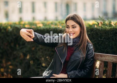 Jolie dame dans une veste en cuir noir avec un sac noir et un chemisier bordeaux. Jolie jeune femme téléphone Banque D'Images