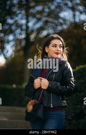 Jolie dame dans une veste en cuir noir avec un sac noir et un chemisier bordeaux. Jeune femme séduisante sourire Banque D'Images