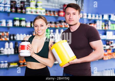Souriant sportif personnes tenant pot en plastique de suppléments alimentaires de sport dans l'intérieur du magasin. Concentrez-vous sur l'homme Banque D'Images